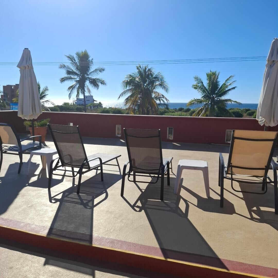 Una terraza en la azotea con mobiliario exterior, palmeras y vista al océano.