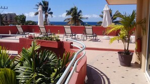 A rooftop terrace with red walls, white umbrellas, and lounge chairs overlooking the ocean.