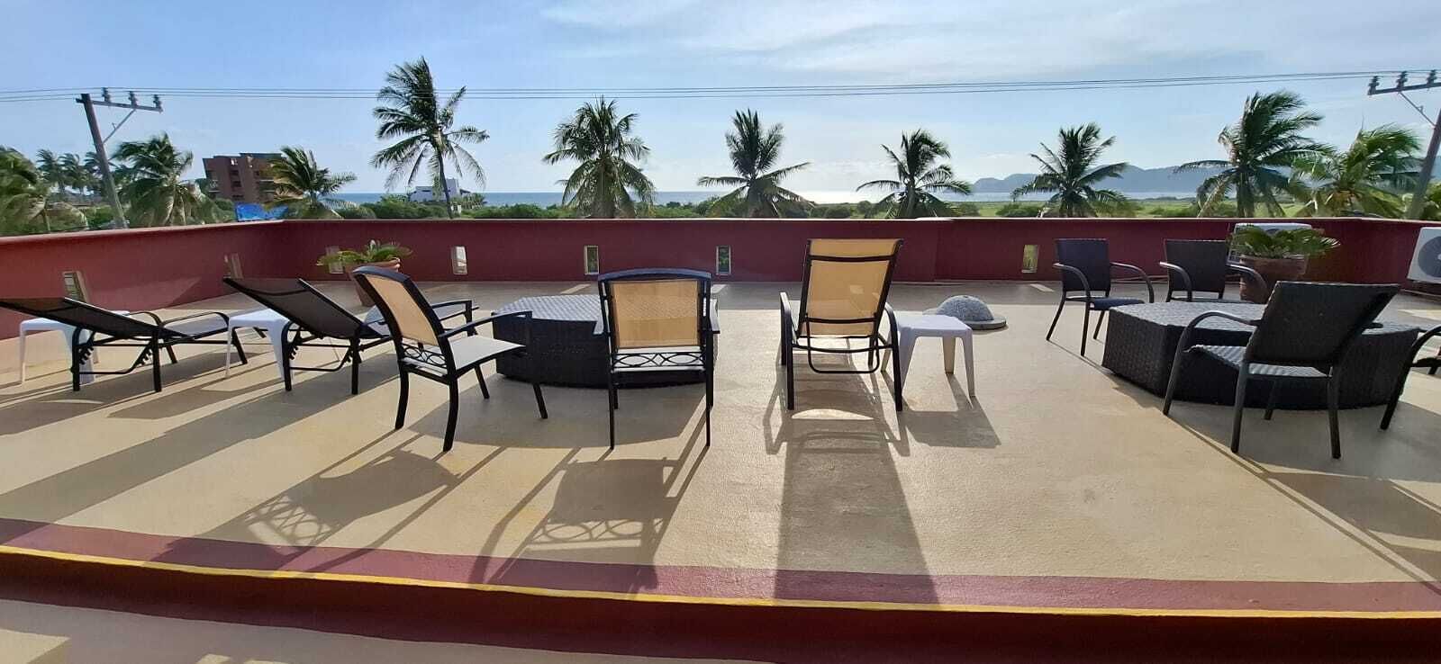 Una terraza en la azotea con mobiliario exterior, palmeras y vistas al océano.