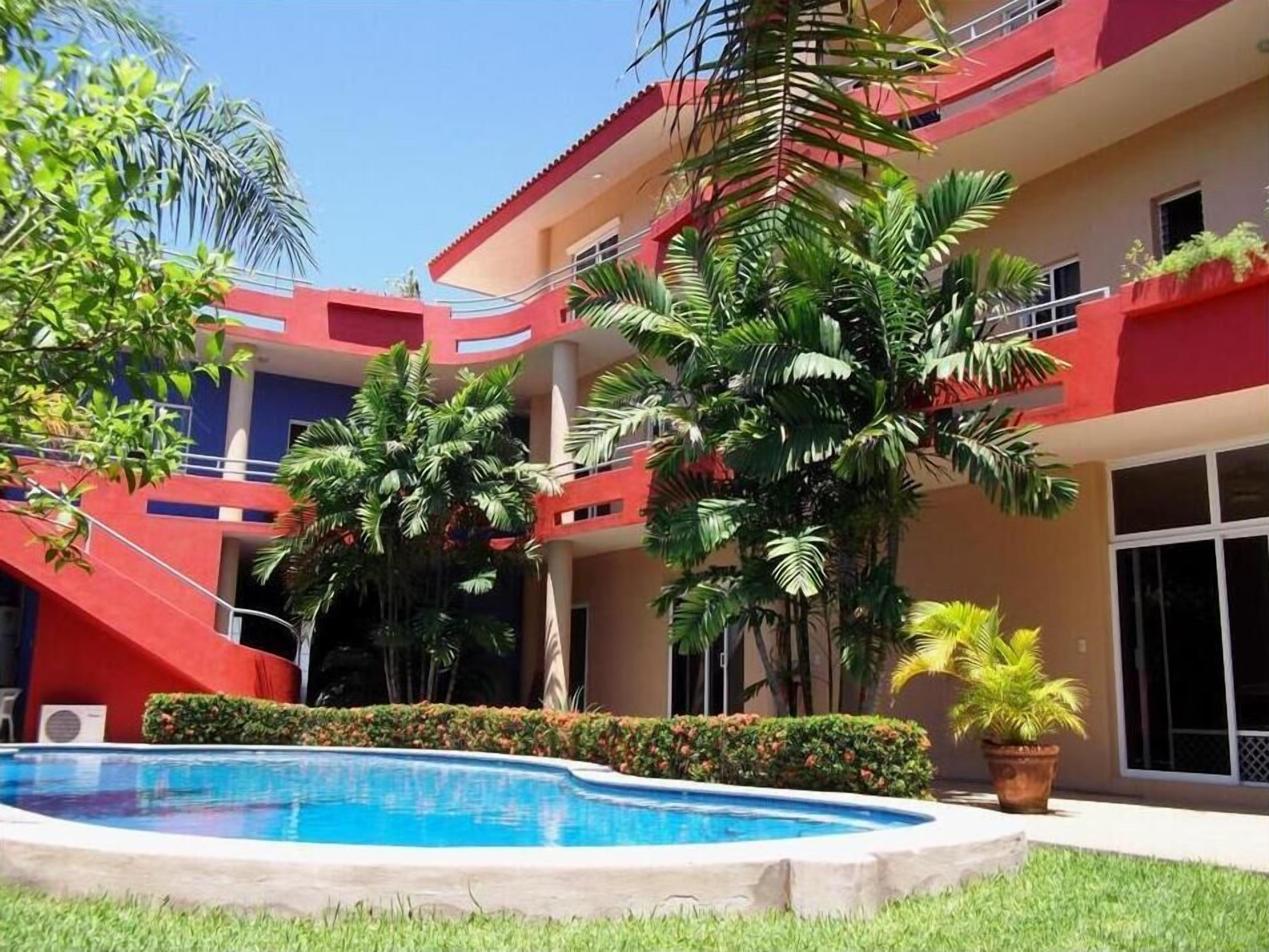 A hotel with a pool, surrounded by lush greenery and palm trees.