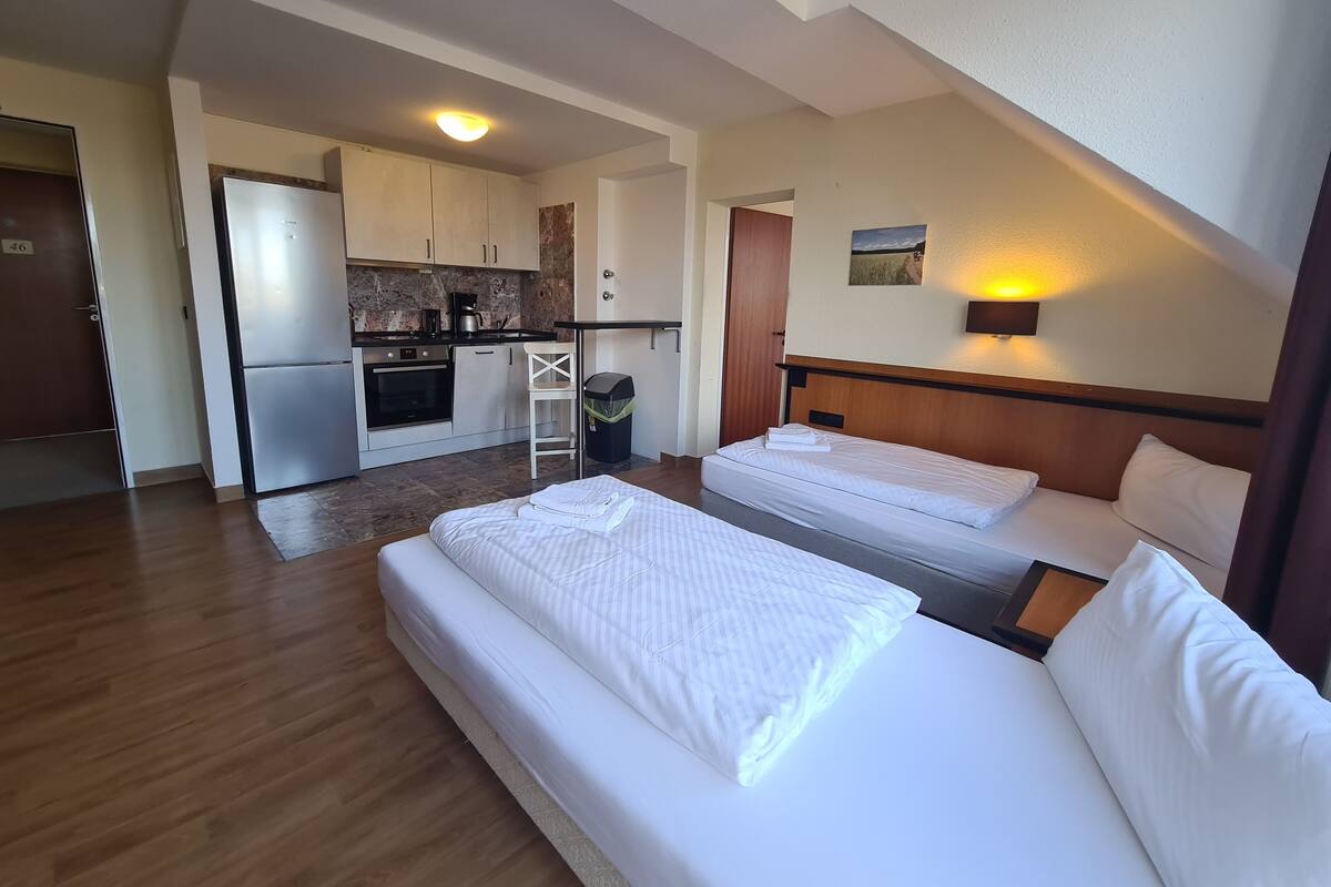 A hotel room with two beds, a kitchenette, and a small dining area.