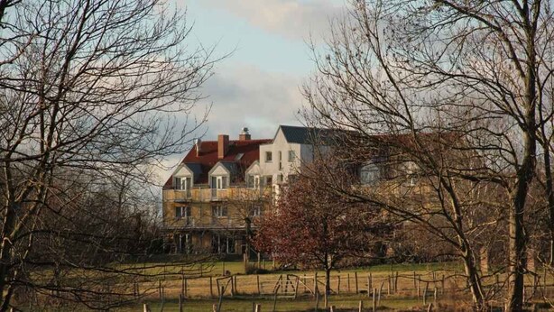 A large, two-story house with a red roof, surrounded by bare trees and a fenced yard. - Landhotel Löwenbruch (Ludwigsfelde)