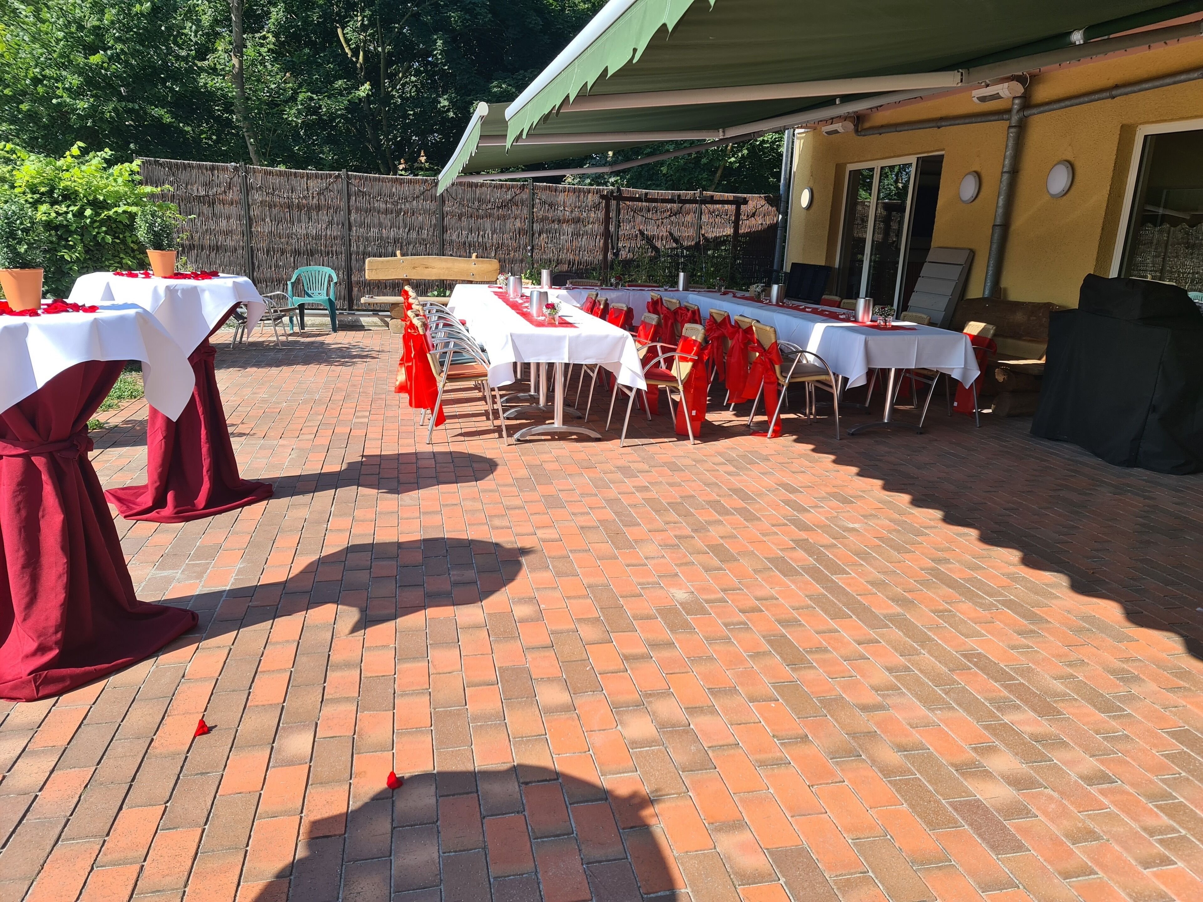 Un'area patio all'aperto con pavimento in mattoni, tavoli con tovaglie bianche e copri-sedie rossi.