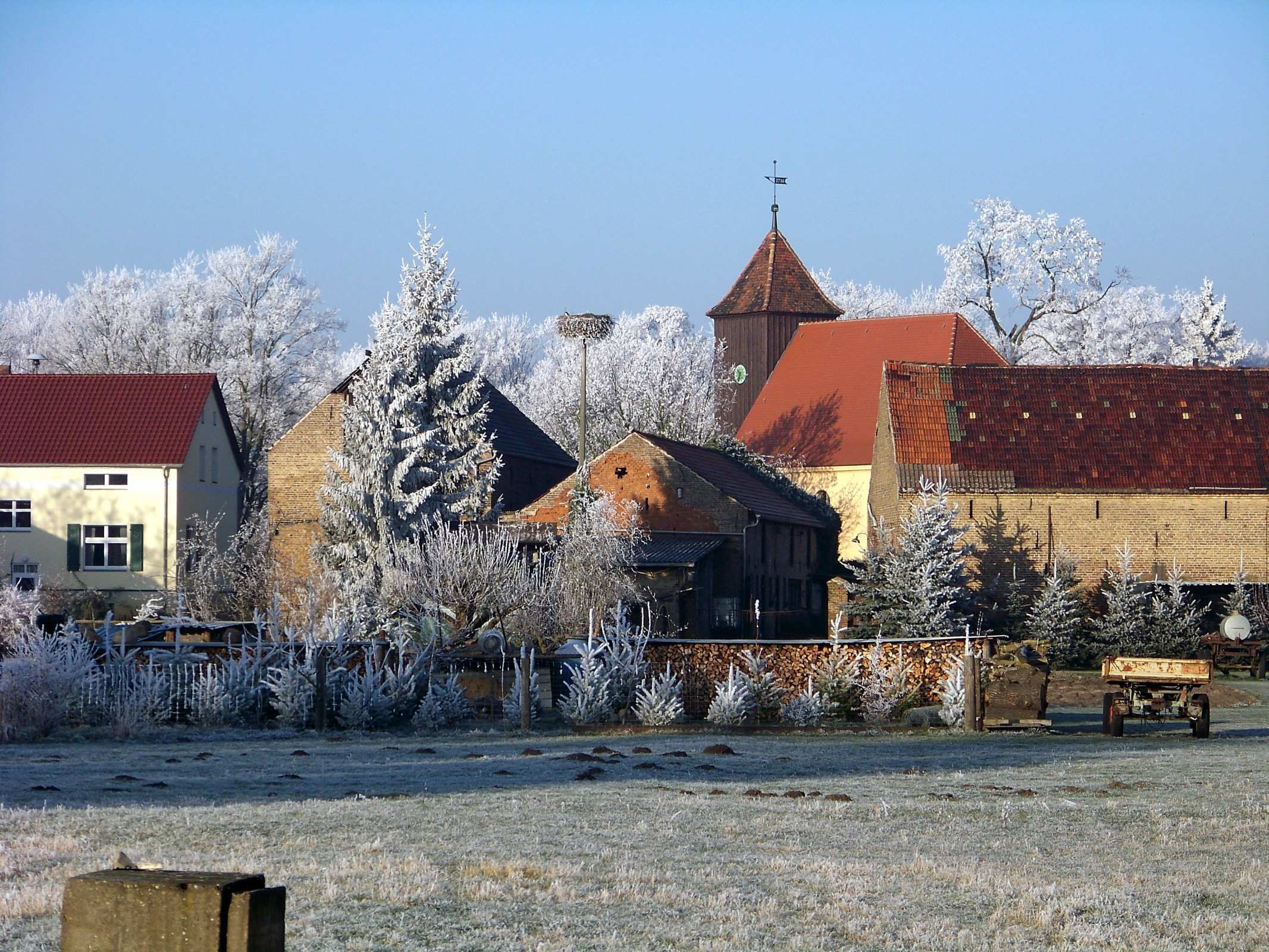 Ein ländliches Dorf mit traditionellen Gebäuden, einer Kirche mit rotem Dach und schneebedeckten Bäumen.