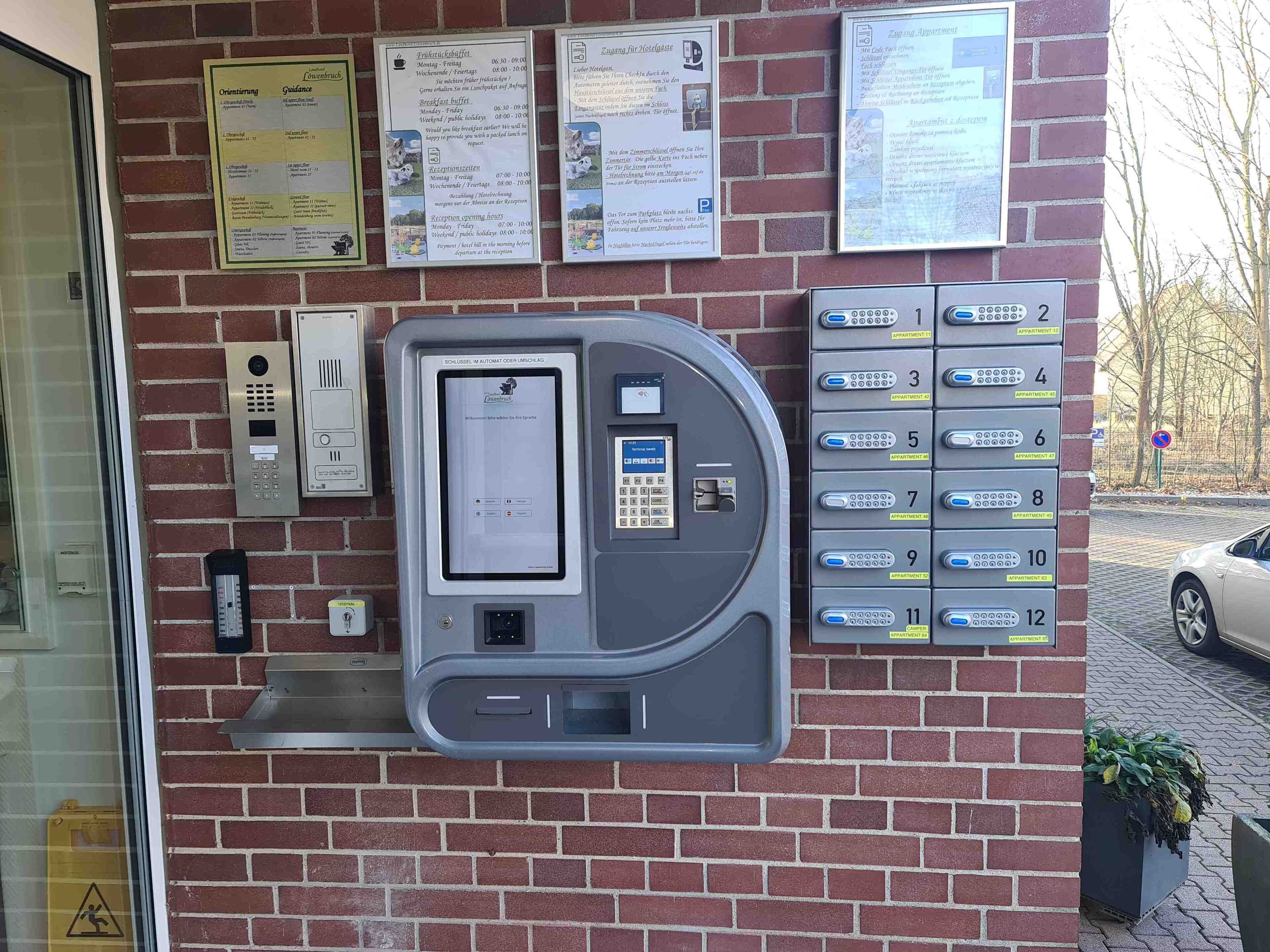 Un espace d’accueil d’hôtel comprenant un kiosque numérique, un téléphone, un détecteur d’incendie et un répertoire indiquant les numéros des appartements.