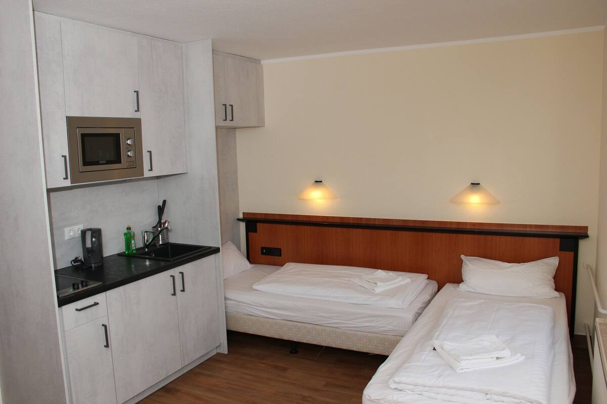 A hotel room with a kitchenette, two beds, and a wooden headboard.