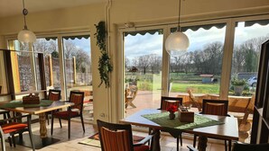 A dining area with tables and chairs, large windows, and hanging lights. - Landhotel Löwenbruch (Ludwigsfelde)