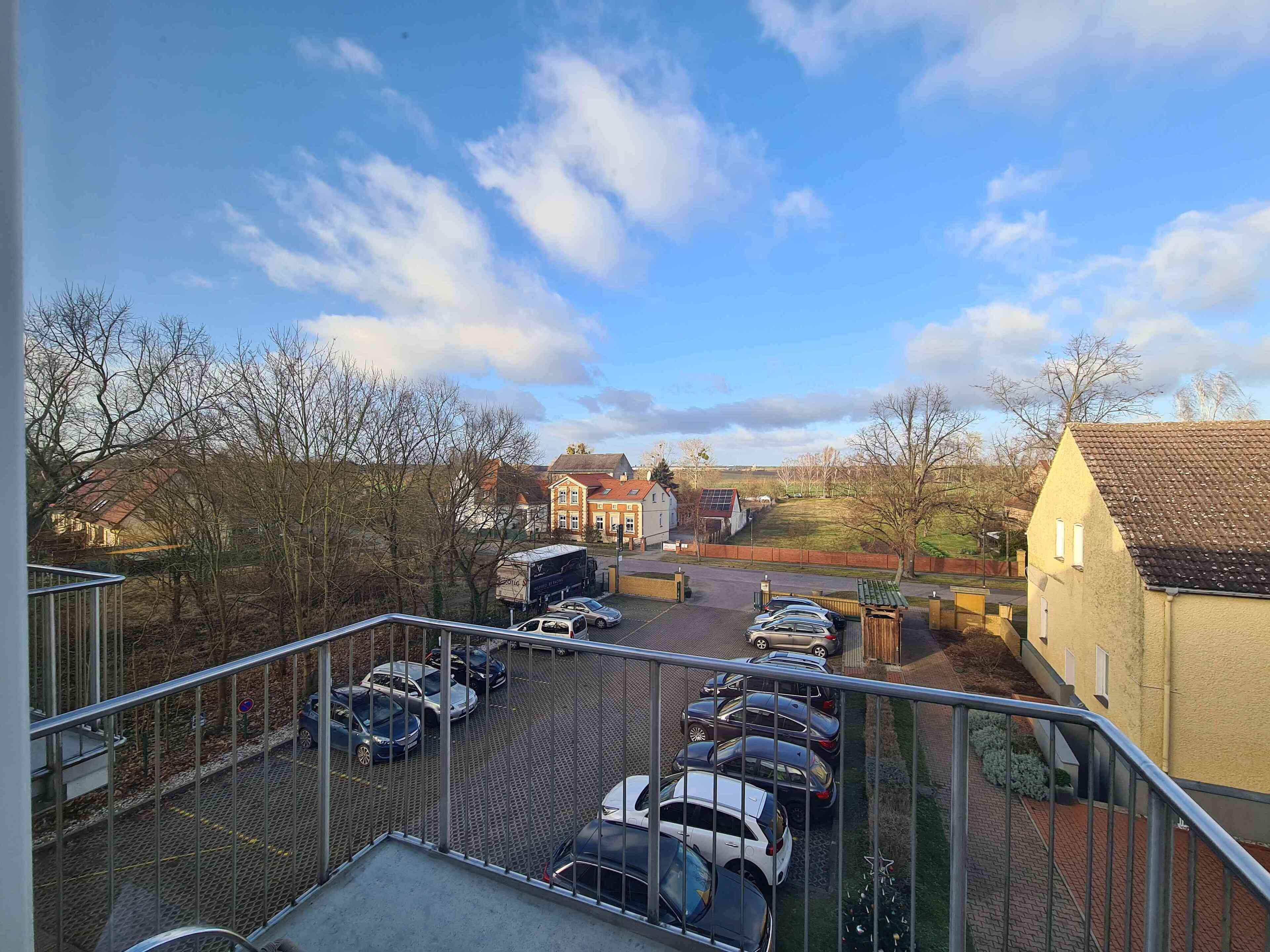 Un parking avec plusieurs voitures, un bâtiment doté d’un toit rouge et un ciel dégagé.