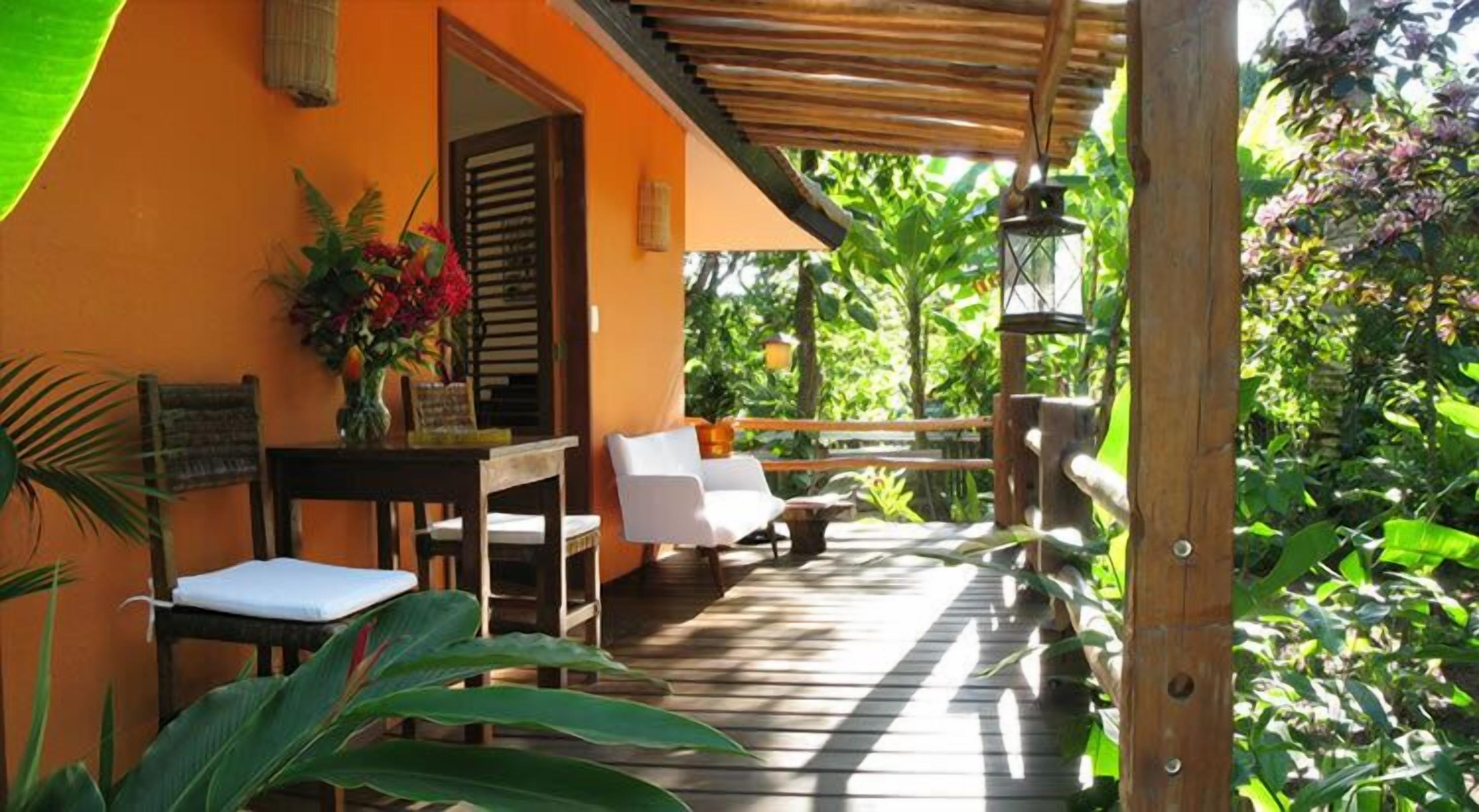 An outdoor wooden deck with a table and chairs, surrounded by lush greenery.