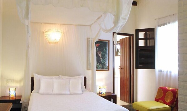 Un dormitorio con cama, lámparas de noche, mesita de noche, una silla y una puerta que da a otra habitación.