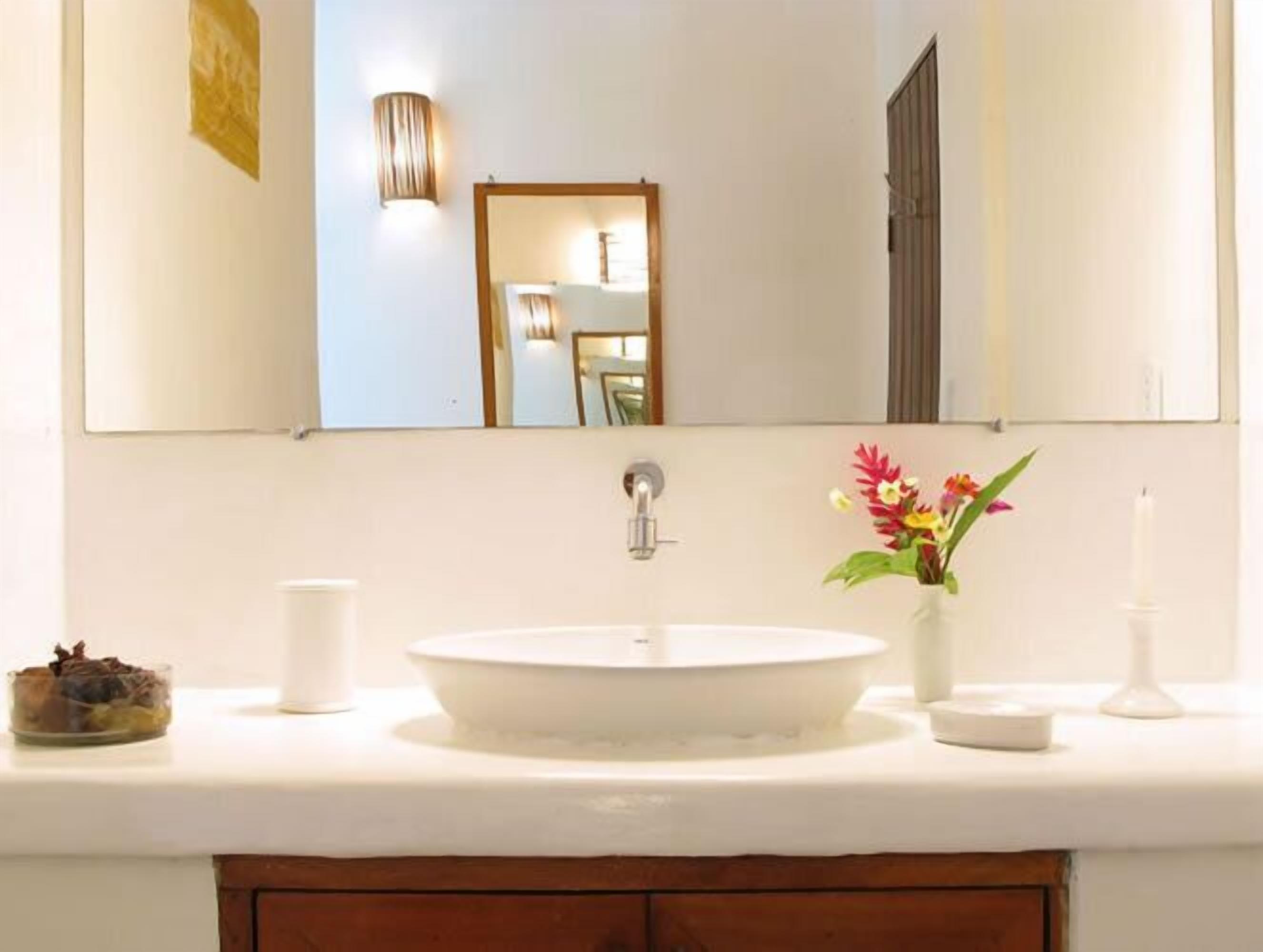 Uma casa de banho com uma pia branca, um espelho e um vaso com flores.
