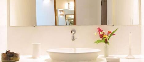 Uma casa de banho com uma pia branca, um espelho e um vaso com flores.