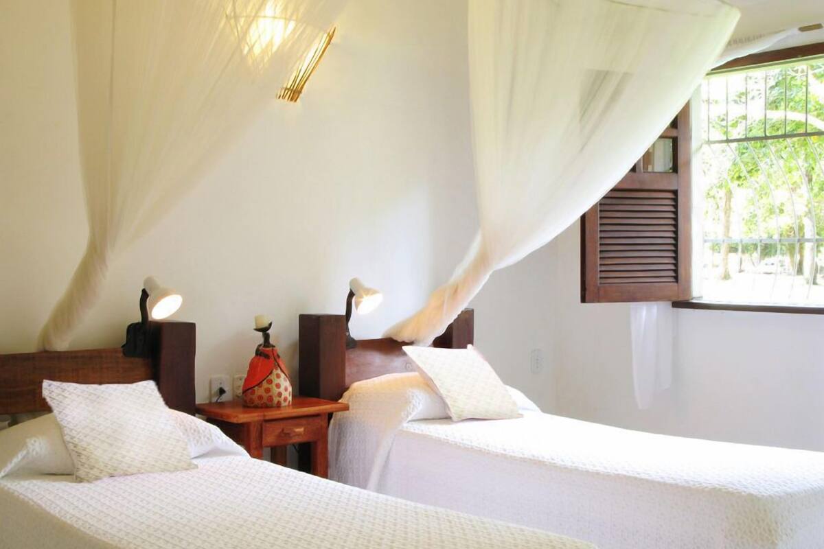 A bedroom with two beds, a nightstand, a lamp, and a window with a view of trees.
