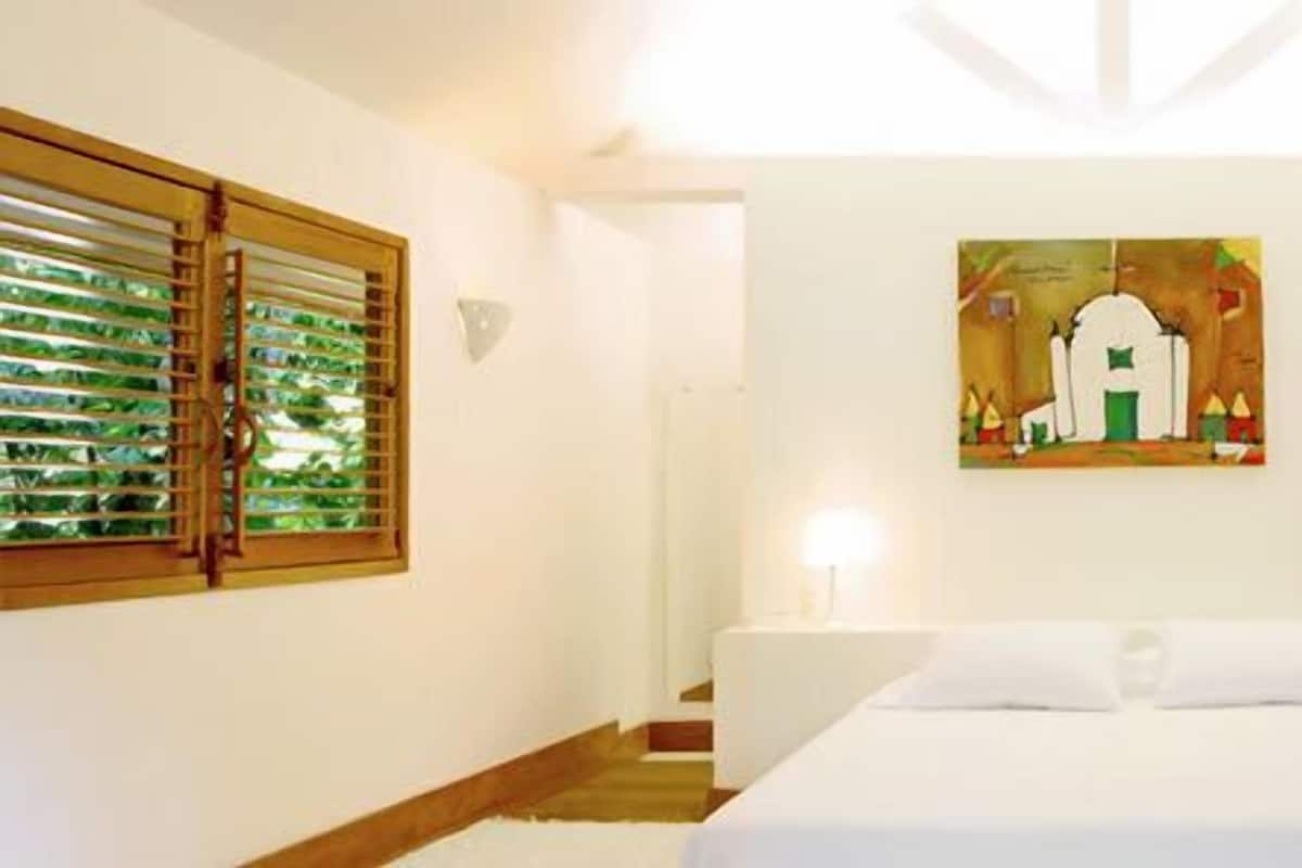 A hotel room with a bed, a painting on the wall, and wooden shutters on the windows.