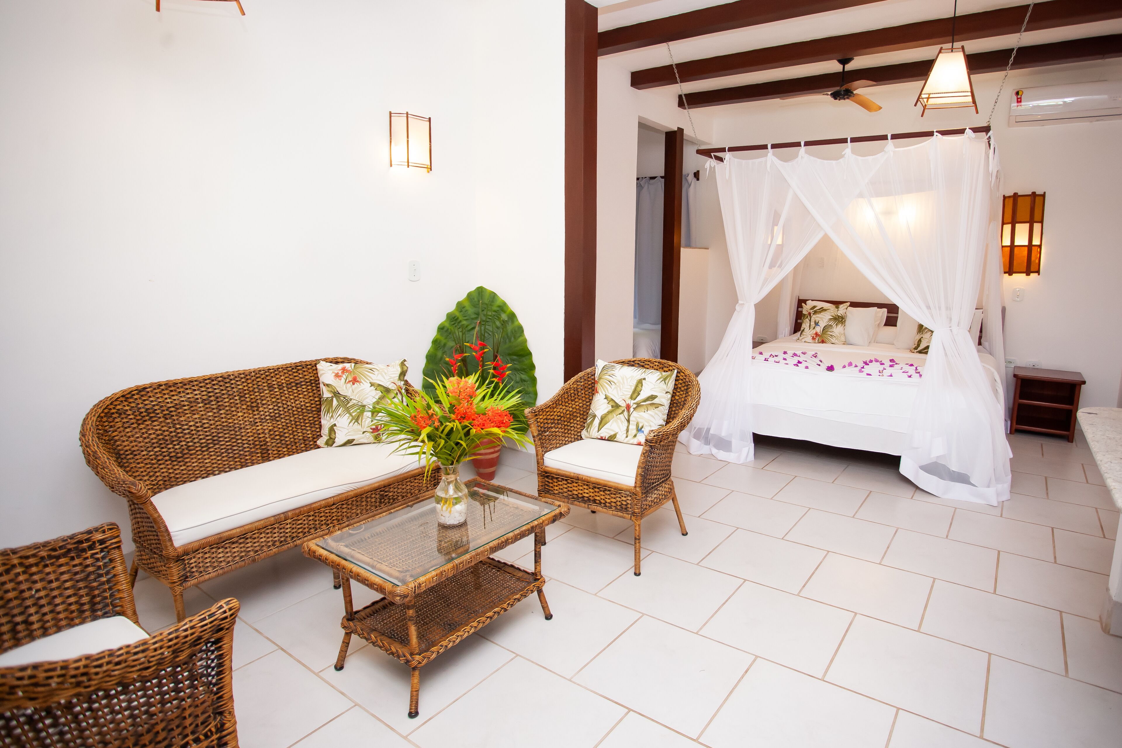 A bedroom with a canopy bed, wicker furniture, and a potted plant.