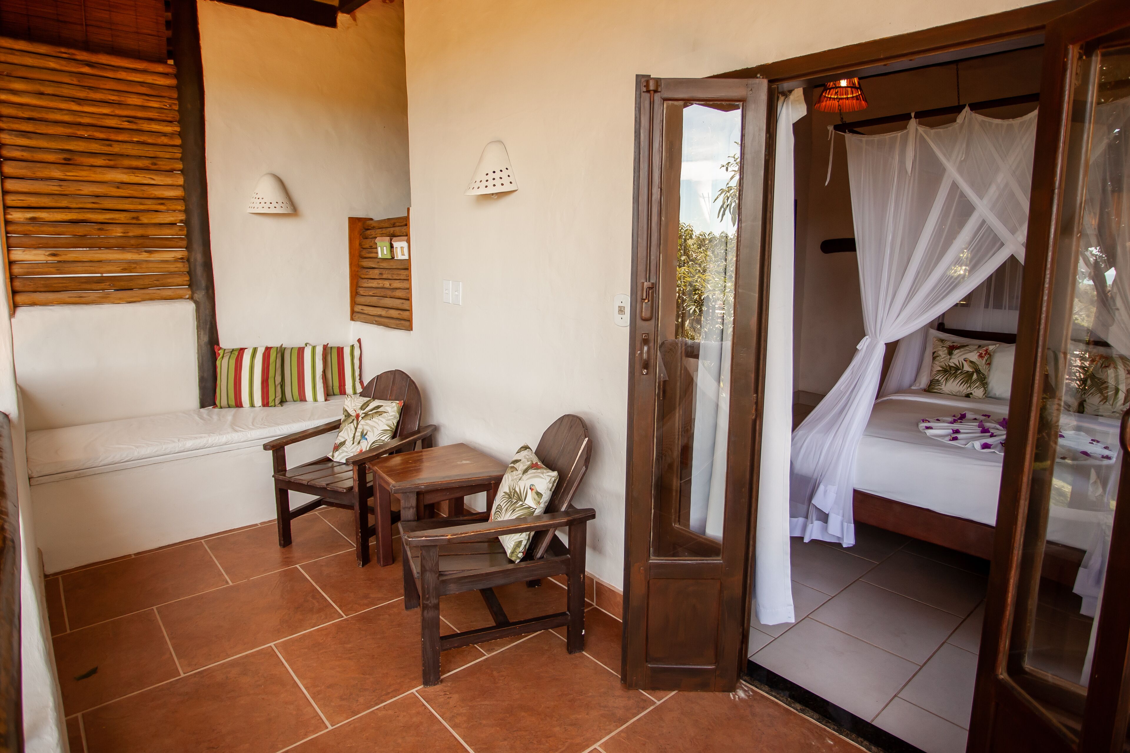 Un dormitorio con una cama, una zona de estar con un banco y sillas, un banco de madera y una puerta que da a otra habitación.