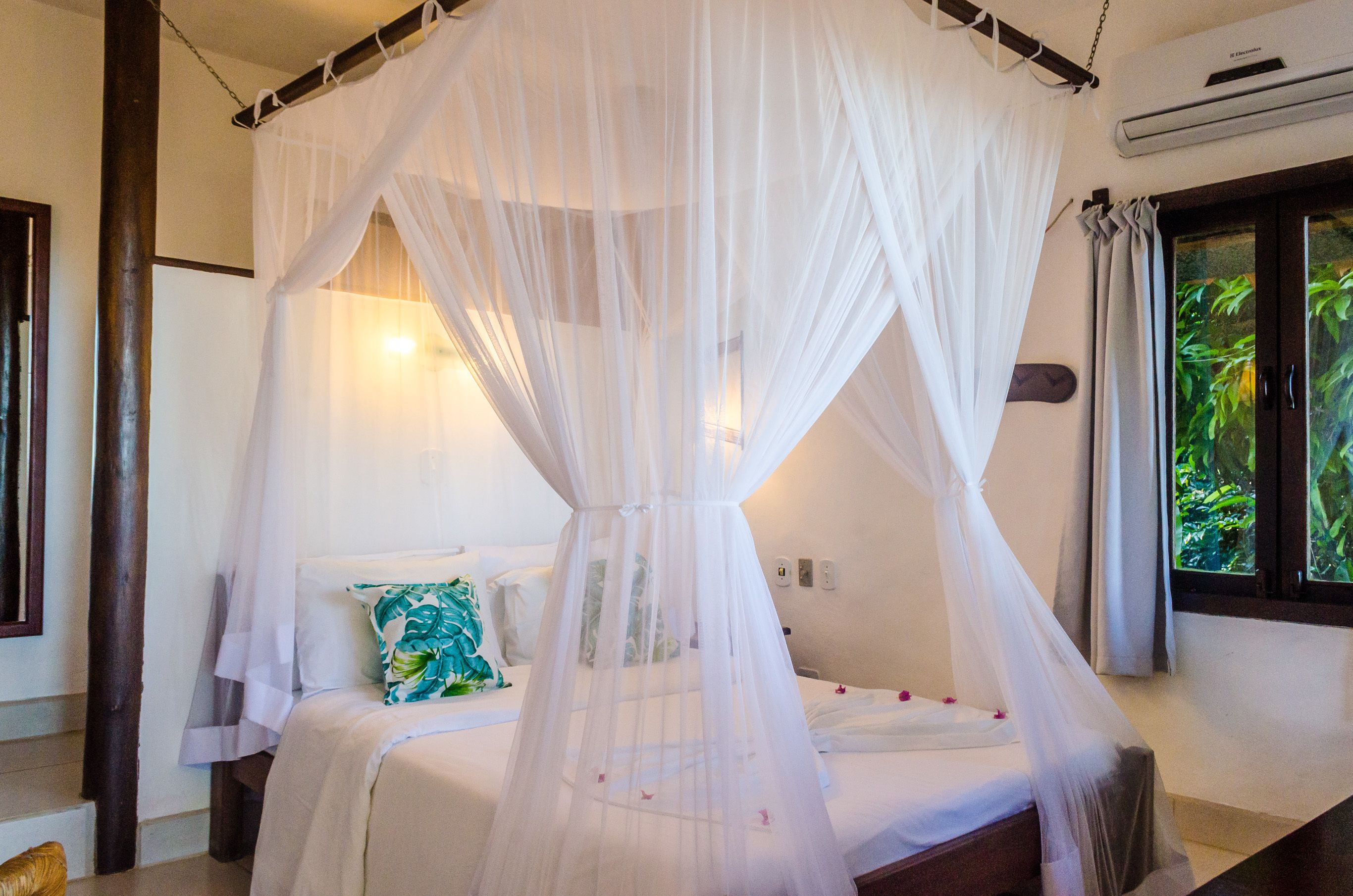 A bed with a white canopy, a pillow with a green leaf pattern, and a window with curtains.