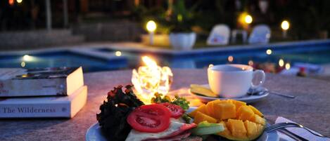 Un plato con comida, una taza y libros sobre una mesa cerca de una piscina.