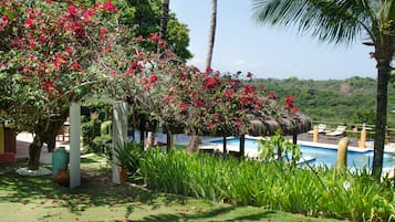 Ein Poolbereich mit weißer Pergola, üppiger Bepflanzung und Blick auf eine hügelige Landschaft.