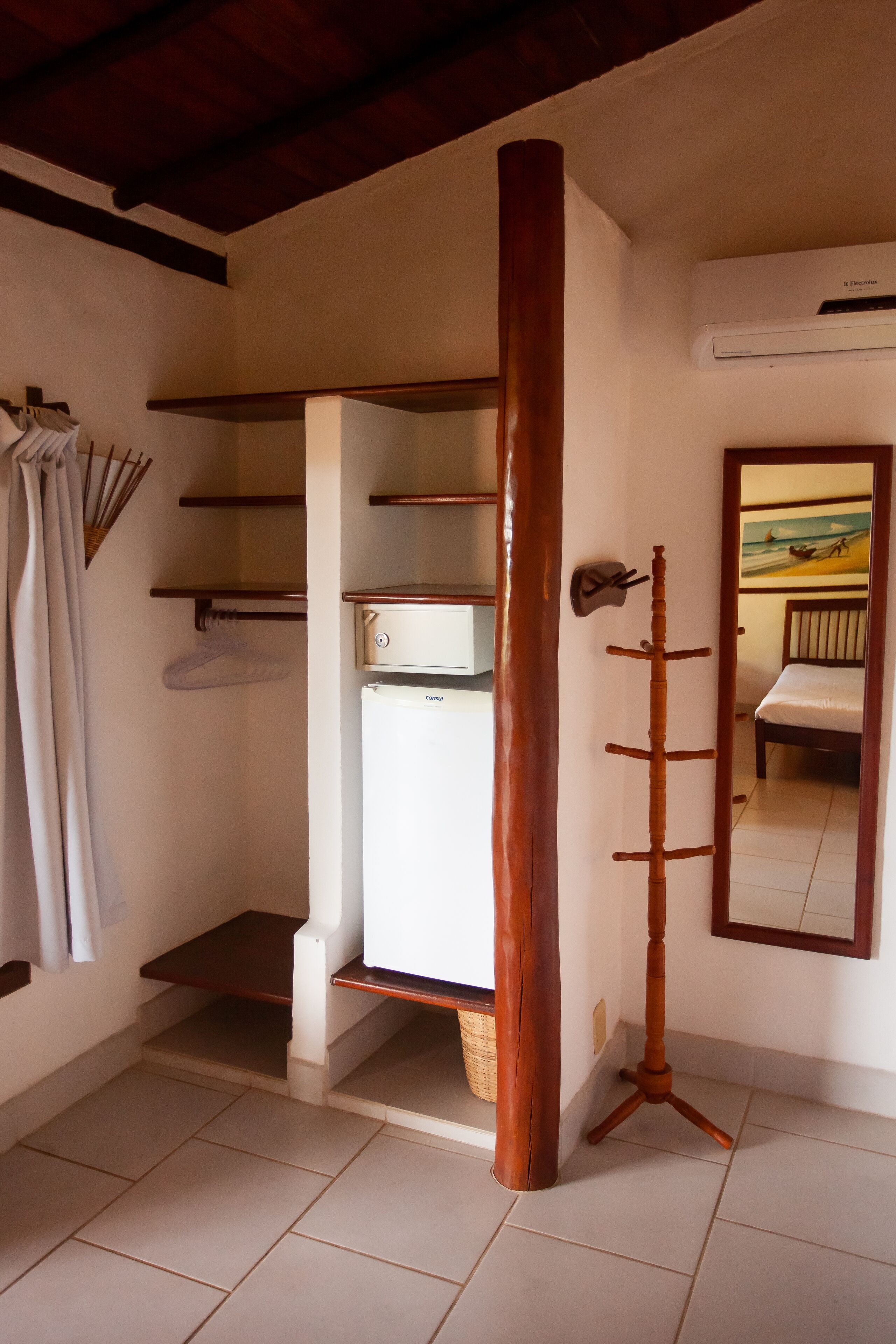 A room with a built-in wardrobe, a wooden coat rack, a bed, and a painting on the wall.