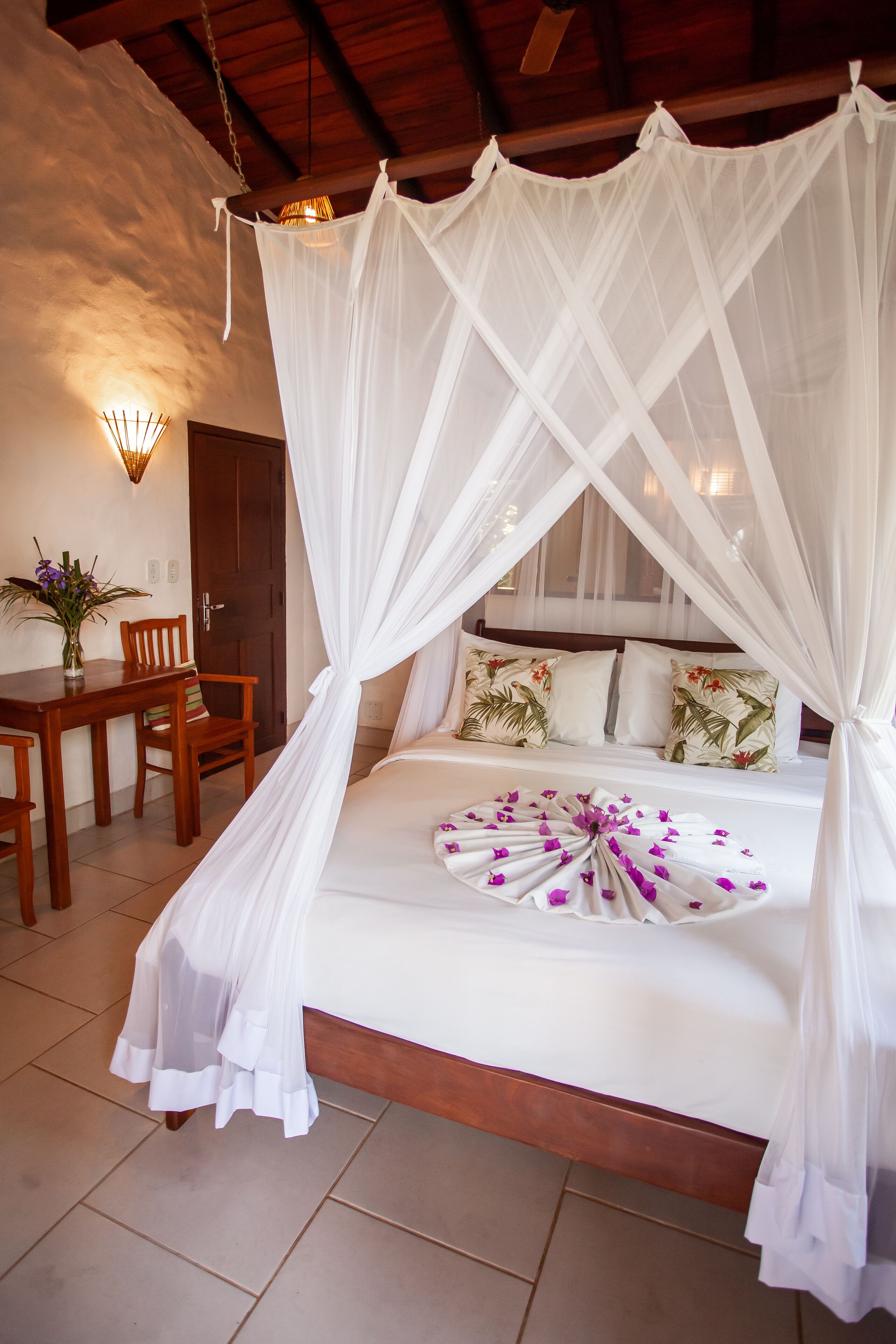 Un dormitorio con una cama con dosel, una mesa de madera, sillas y un jarrón con flores.