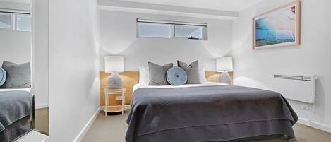 Een moderne slaapkamer met een groot bed, een nachtkastje, een raam en een schilderij aan de muur.