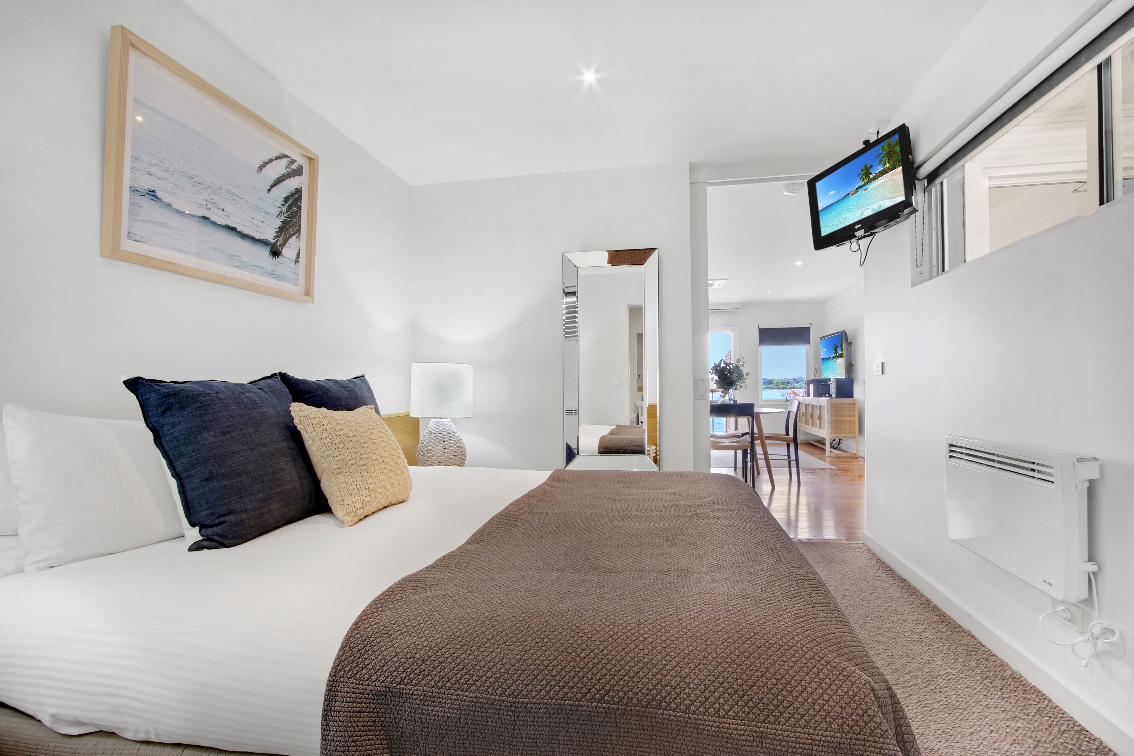 Ein modernes Hotelzimmer mit einem großen Bett, einem an der Wand befestigten Fernseher und Meerblick durch das Fenster.