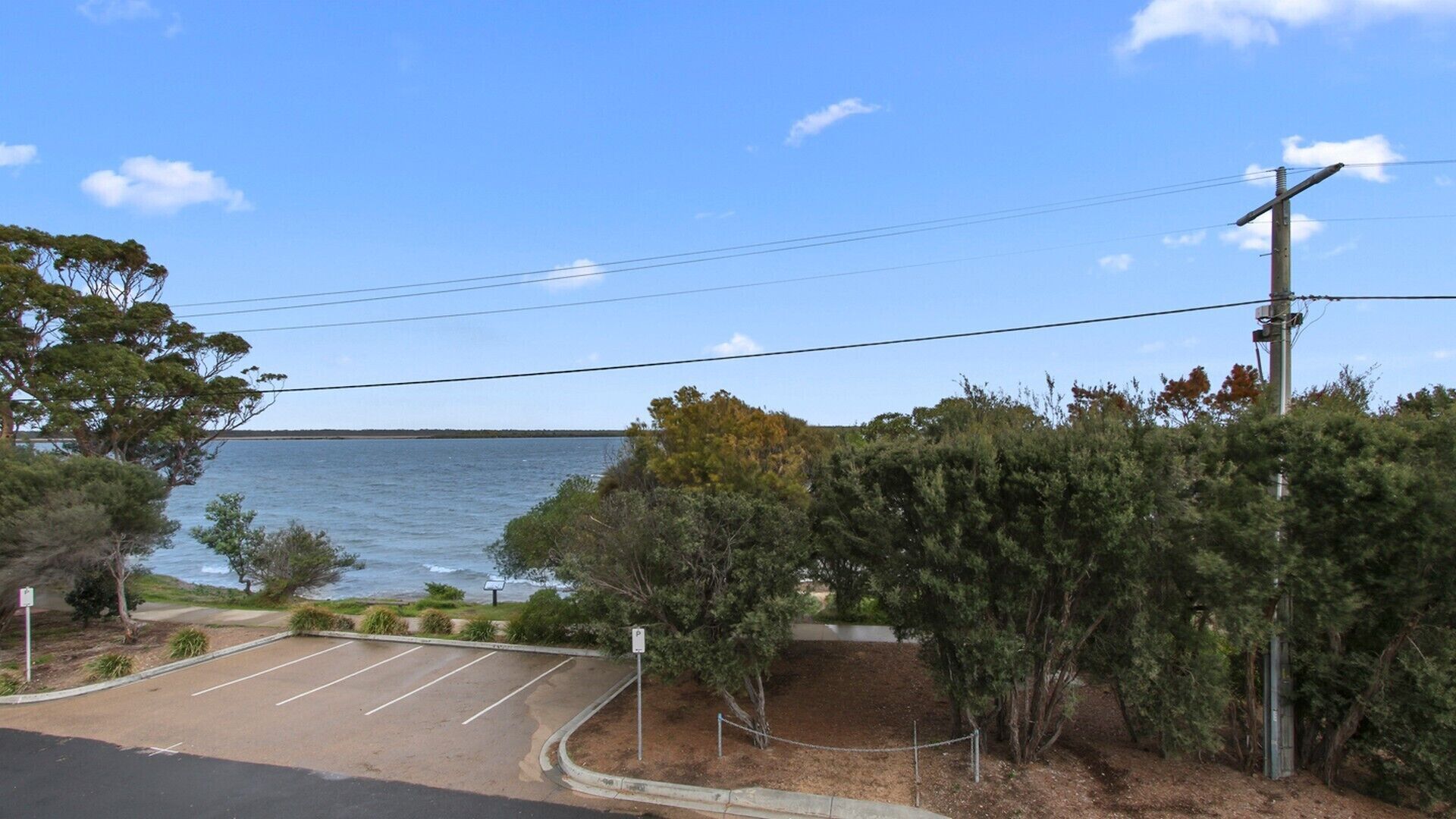 A parking lot with a view of the sea, surrounded by trees and a utility pole.