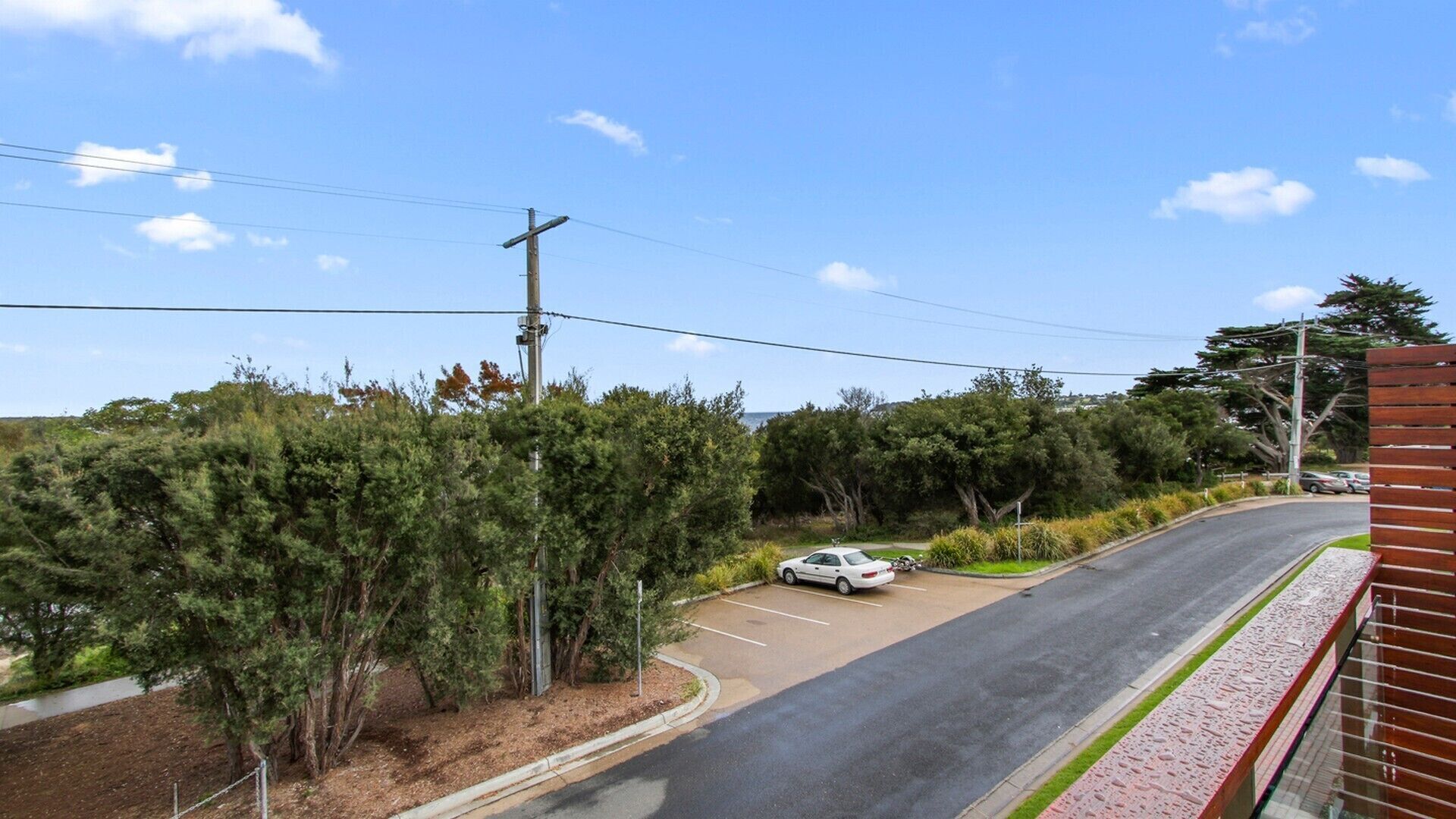 A parking lot with a white car, surrounded by dense greenery and a clear sky.
