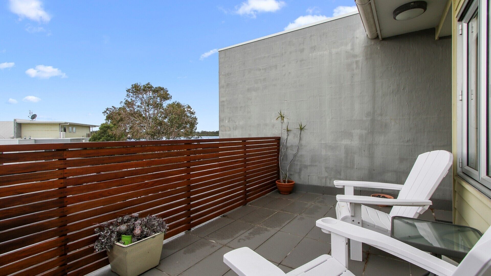 A balcony with a wooden fence, a potted plant, and a white chair.