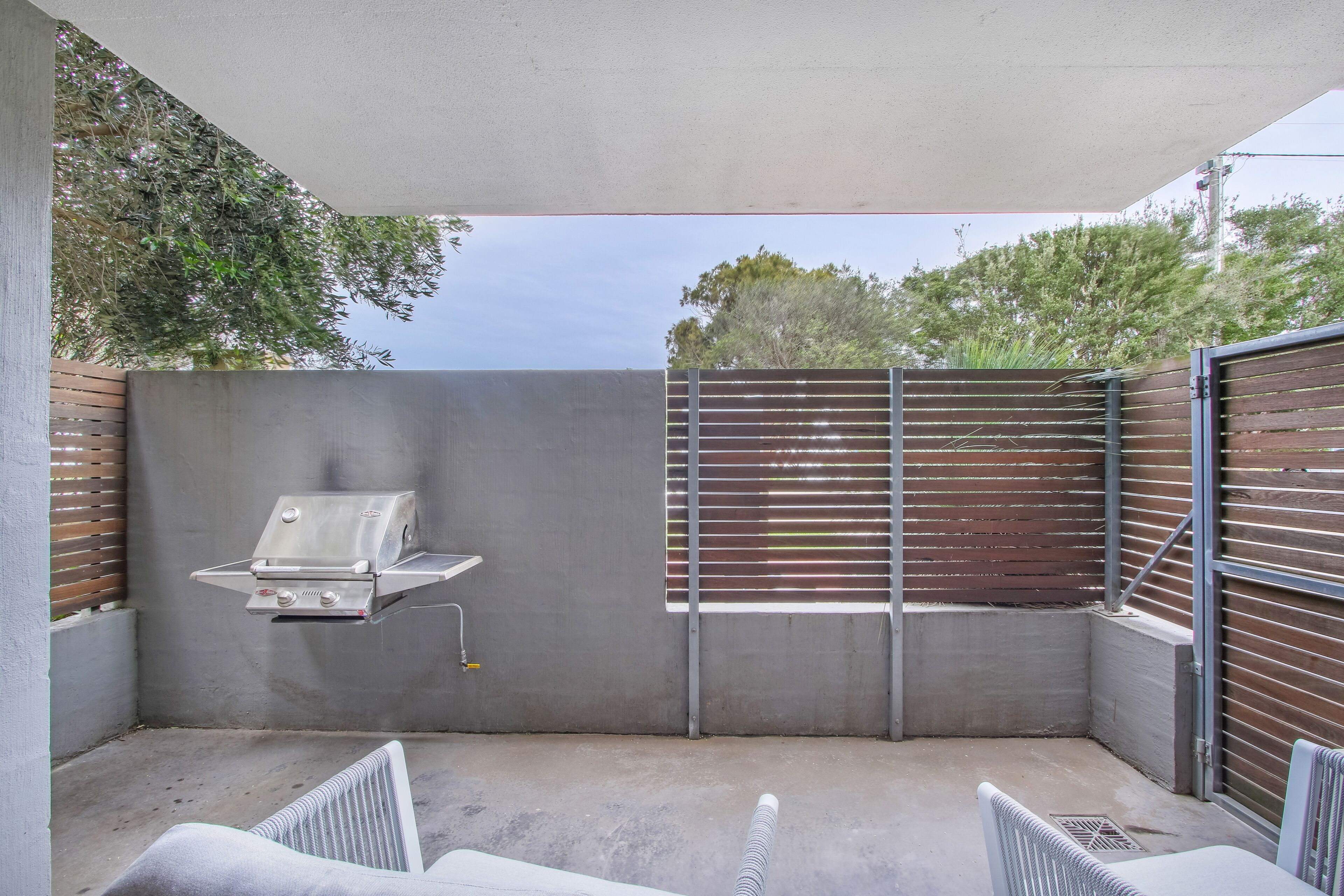 An outdoor patio with a built-in grill, seating area, and a view of the sky and trees.