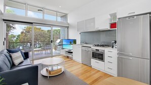 Cocina moderna con refrigerador Bosch, lavavajillas y estufa. Hay un comedor con mesa y sillas, y un balcón con vista a árboles.
