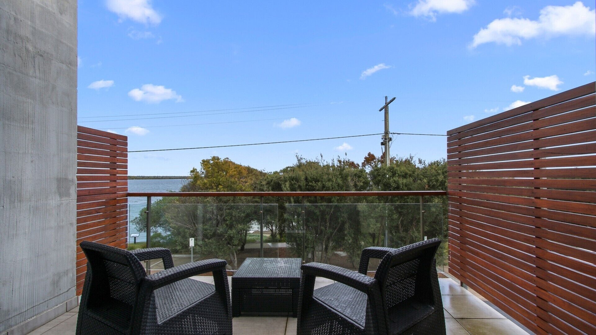 A balcony with wicker furniture, a glass barrier, and a view of trees and a power line.