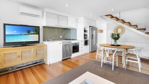 Una cocina moderna con un televisor grande, armarios de madera y un comedor con sillas blancas.