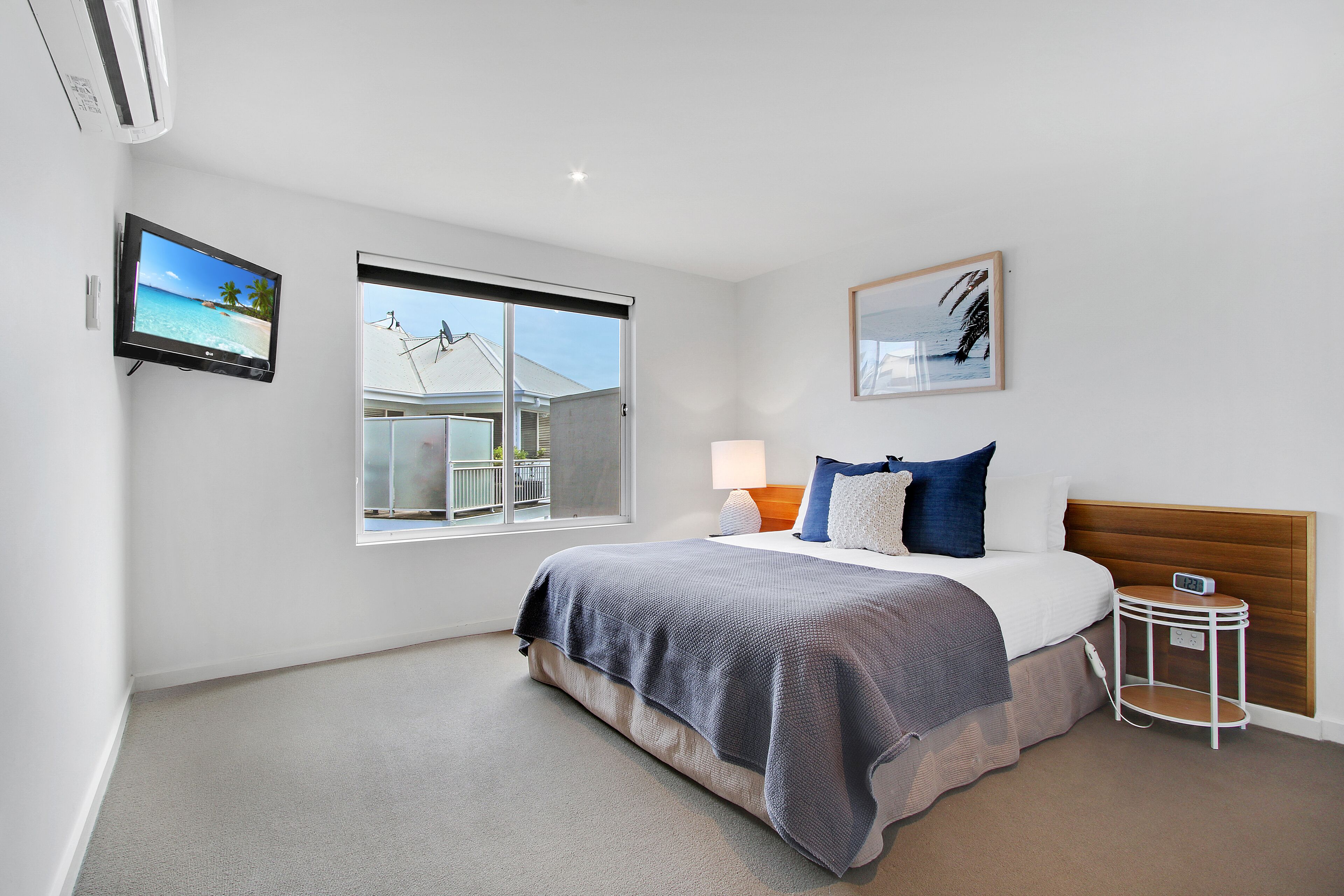 A modern bedroom with a large bed, a TV, a window with a view, and a bedside table with a lamp.
