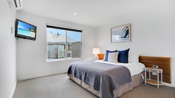 A modern bedroom with a large bed, a TV, a window with a view, and a bedside table with a lamp.