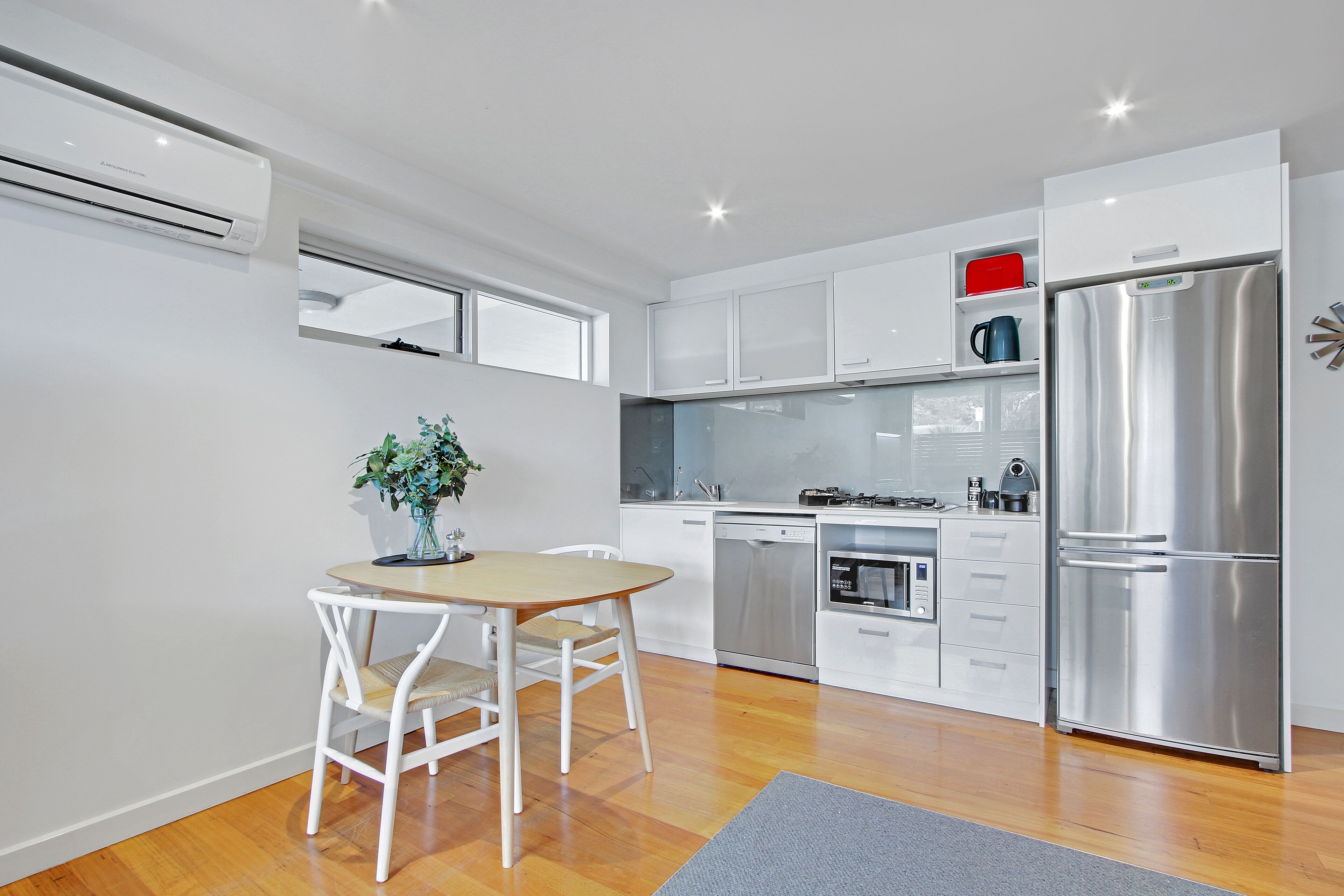 A modern kitchen with white cabinetry, a stainless steel refrigerator, and a dining area with a wooden table and chairs.