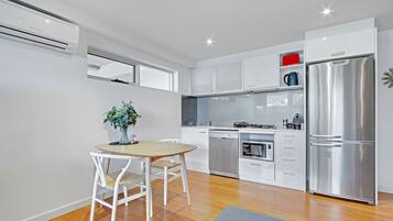 A modern kitchen with white cabinetry, a stainless steel refrigerator, and a dining area with a wooden table and chairs.