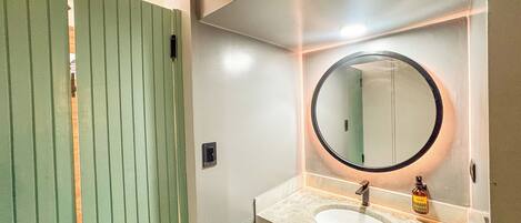 A bathroom with a green door, a round mirror, a sink, and a bottle of hand soap.