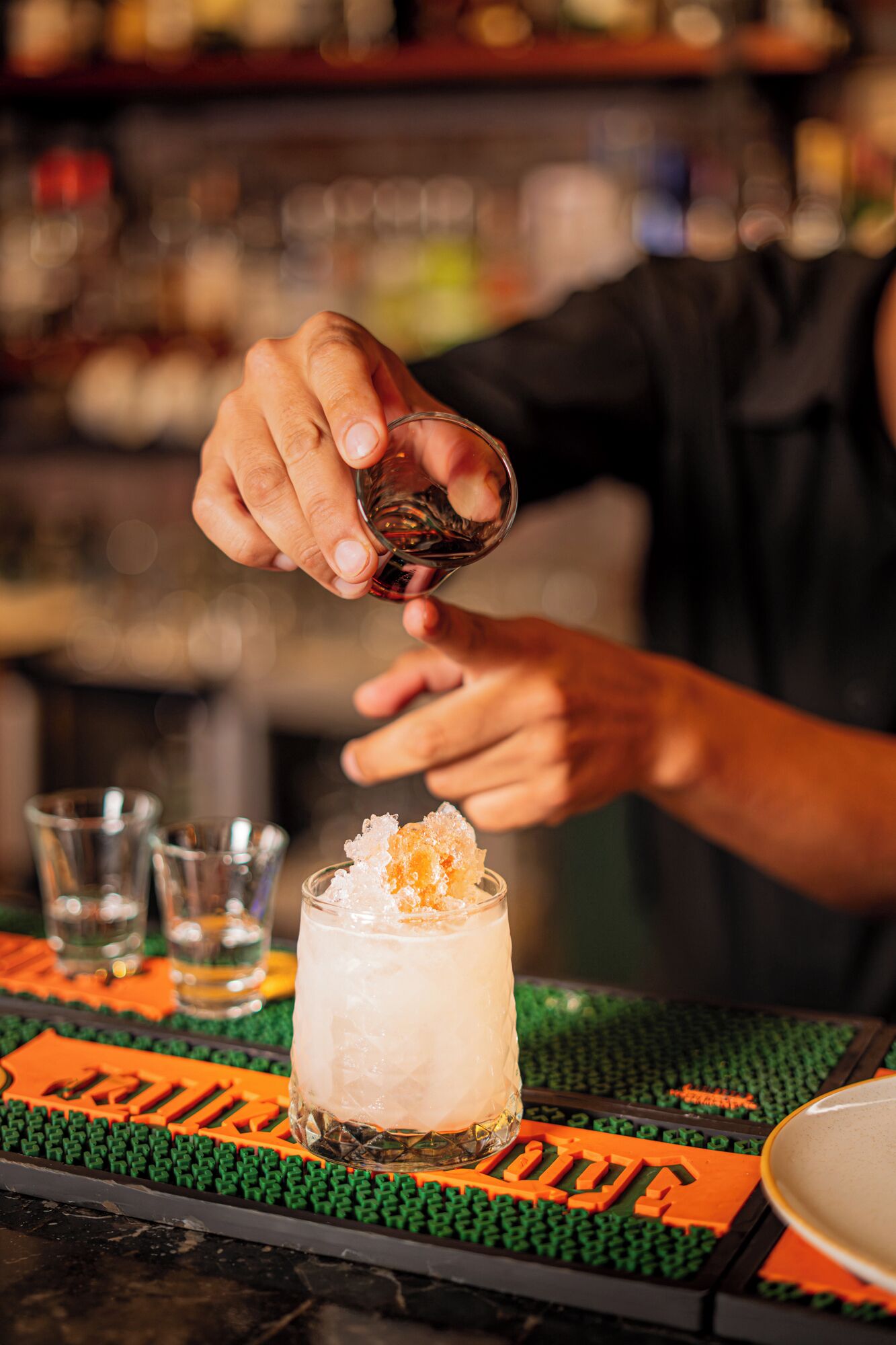 Un bartender sirviendo una bebida en un vaso con hielo y una guarnición.