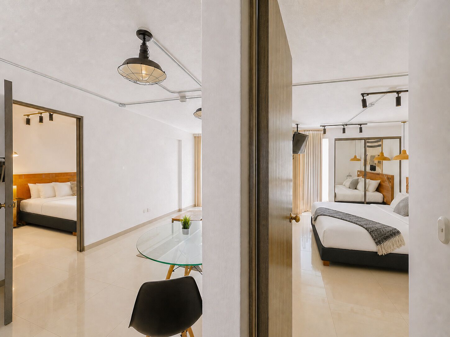 Ett hotellrum med en säng, ett glasbord med en stol, en liten växt och en dörr som leder till ett annat rum.