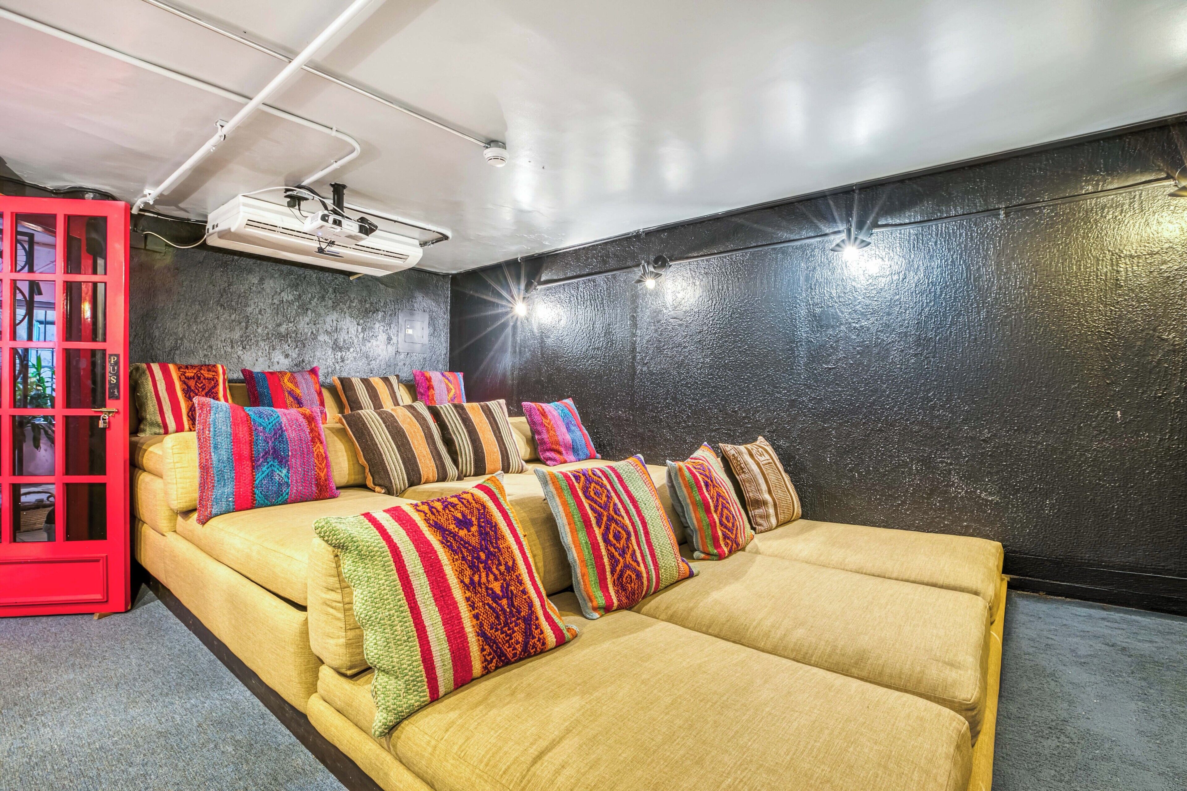 Una habitación con sofá cama, almohadas coloridas, un aparador rojo y un proyector en el techo.