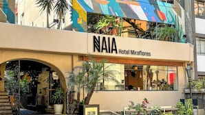 Een hotelgebouw met een kleurrijke gevel, een bord waarop 'NAIA Hotel Miraflores' staat en een duidelijke entree met treden die naar de deur leiden.