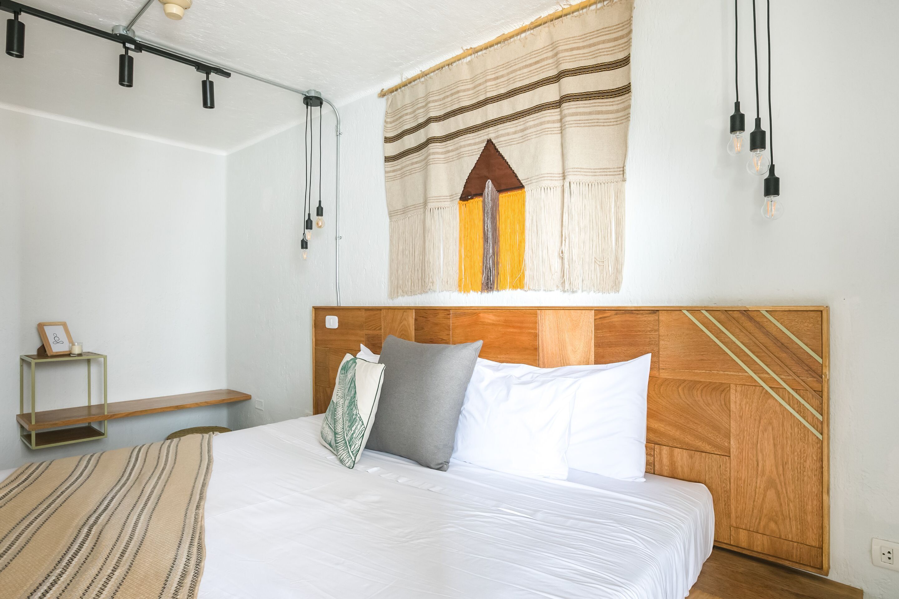 A neatly made bed with a wooden headboard, a bedside table with a lamp, and a wall-mounted artwork above the bed.