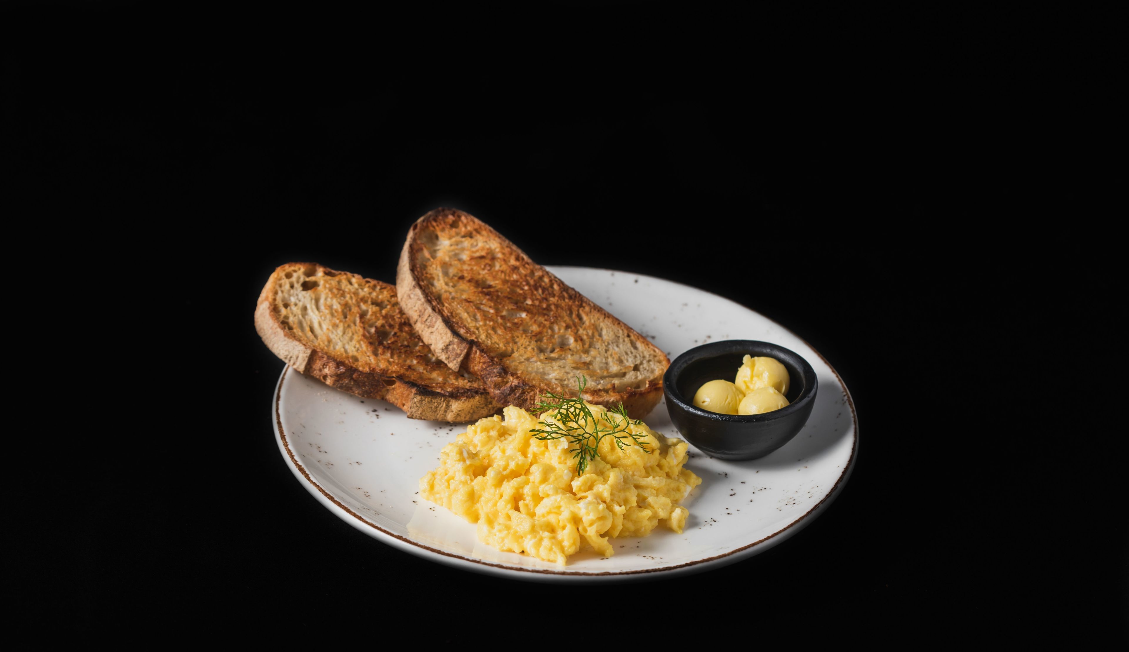 A plate with scrambled eggs, toasted bread, and a small bowl of butter.