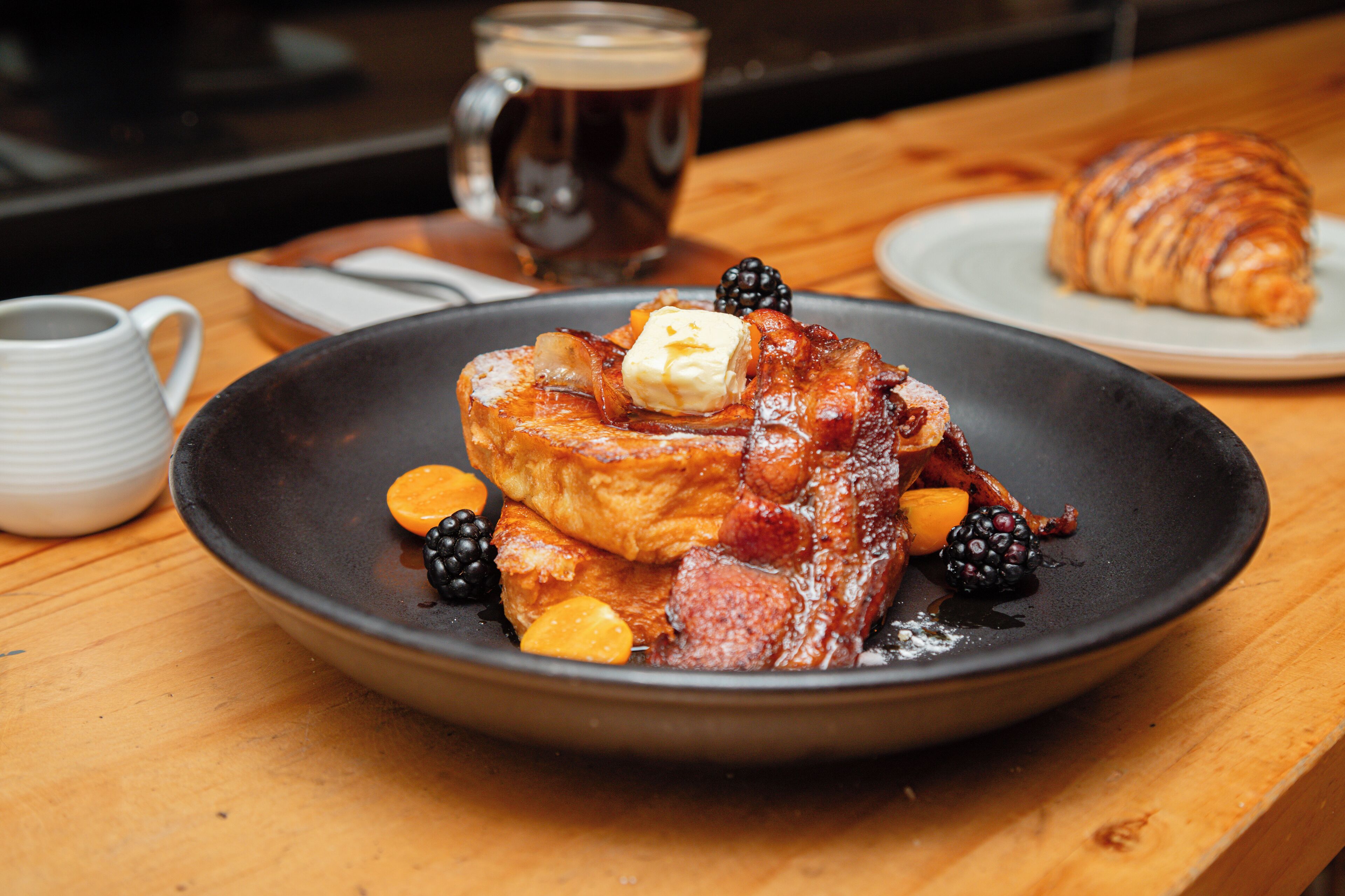 A breakfast plate with toast, butter, bacon, and berries on a wooden table.