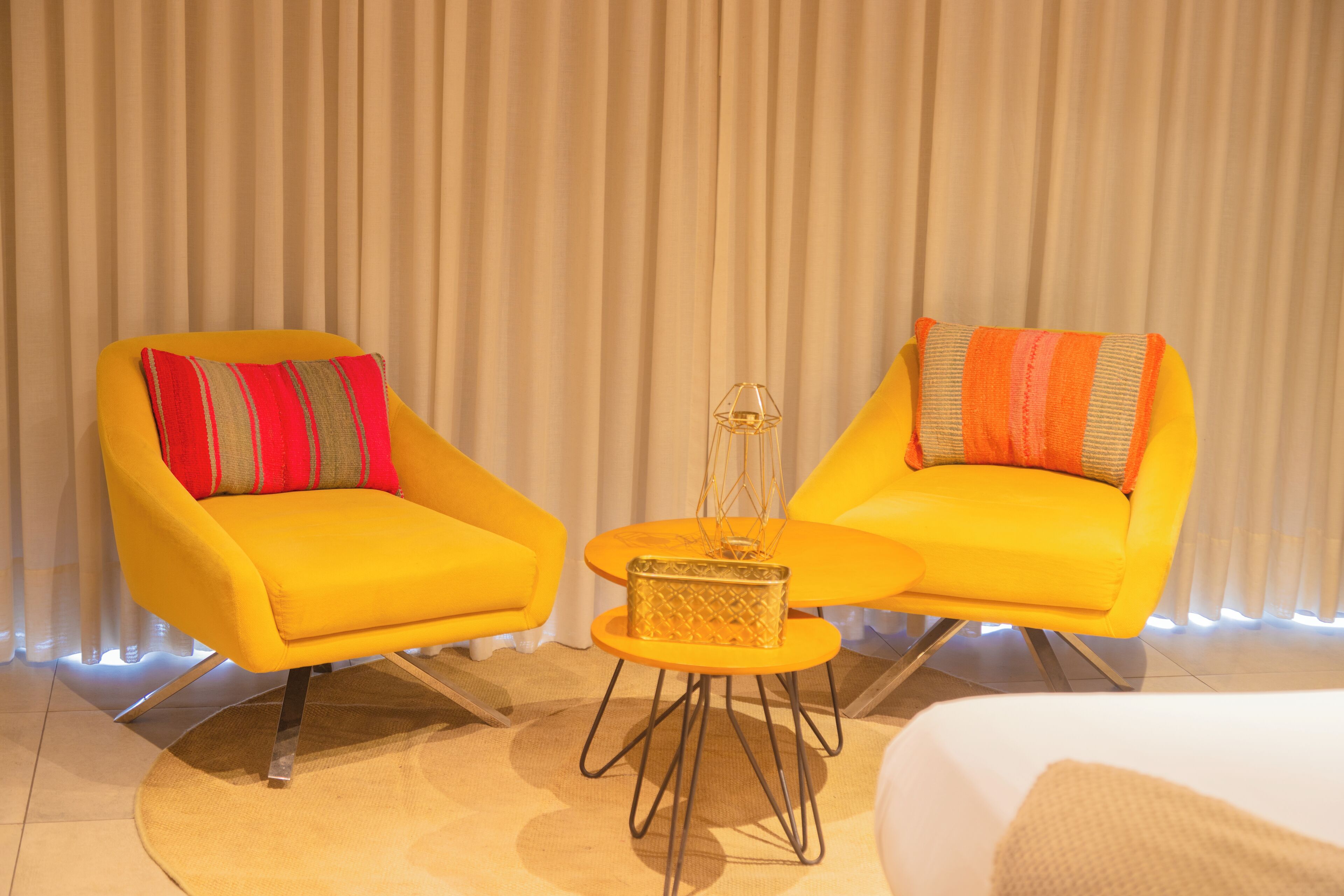 Une pièce avec deux fauteuils jaunes, une petite table ronde agrémentée d’un objet décoratif et un lit à l’arrière-plan.