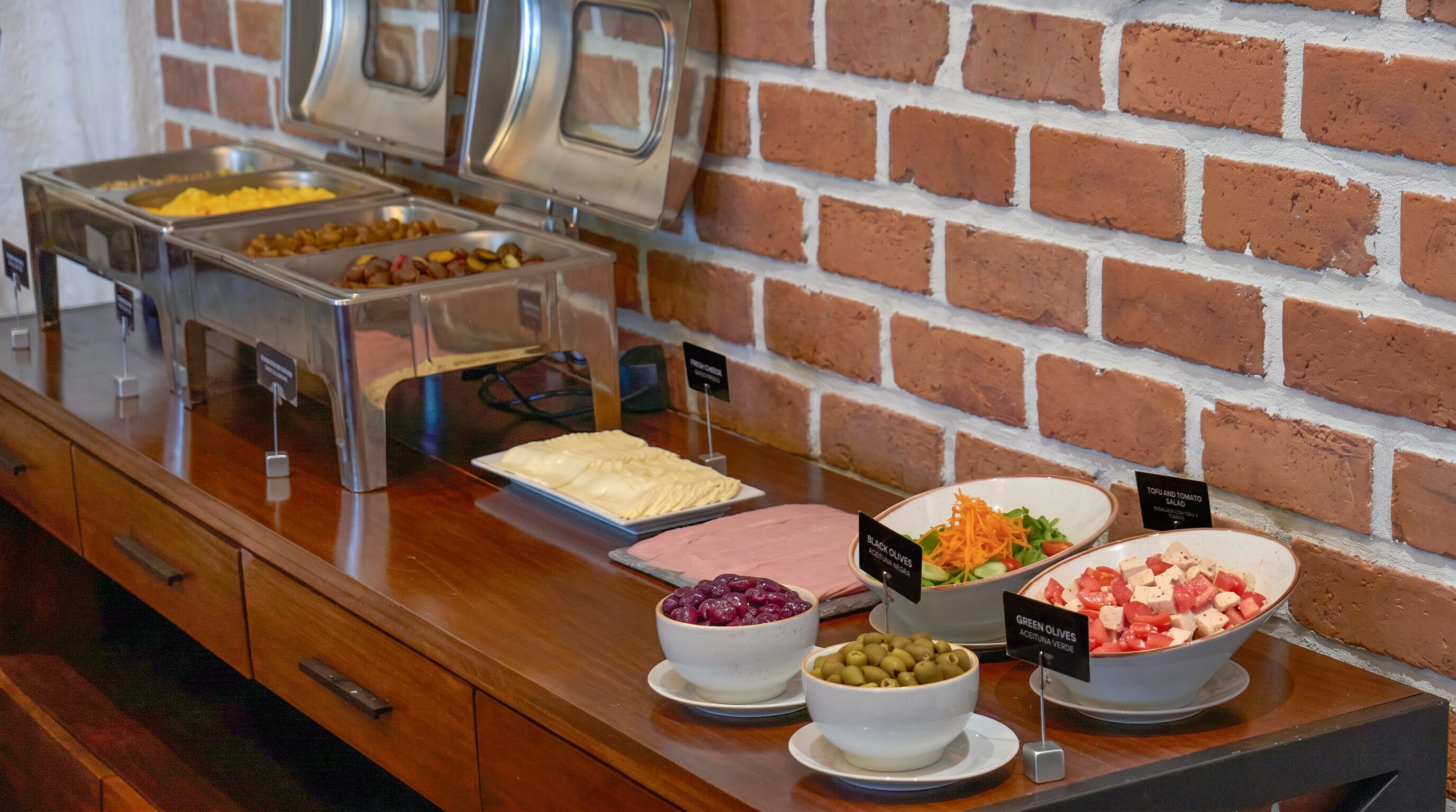 A buffet with various food options, including salads and meats, displayed on a counter with a brick wall background.