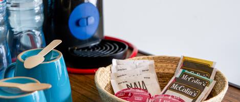 A coffee maker, blue cups, and a basket with McColin's coffee packets on a wooden surface.
