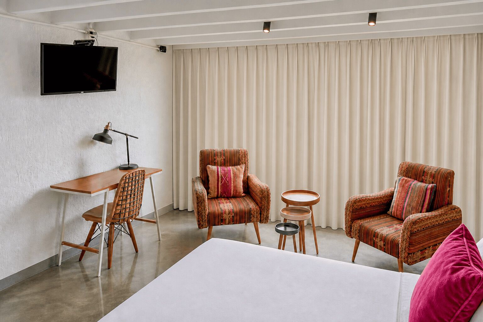 A hotel room with a bed, two armchairs, a desk, and a television.